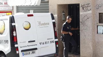 Un agente de la Policía Nacional junto a una furgoneta de los servicios funerarios en el domicilio de la mujer fallecida en Alcorcón