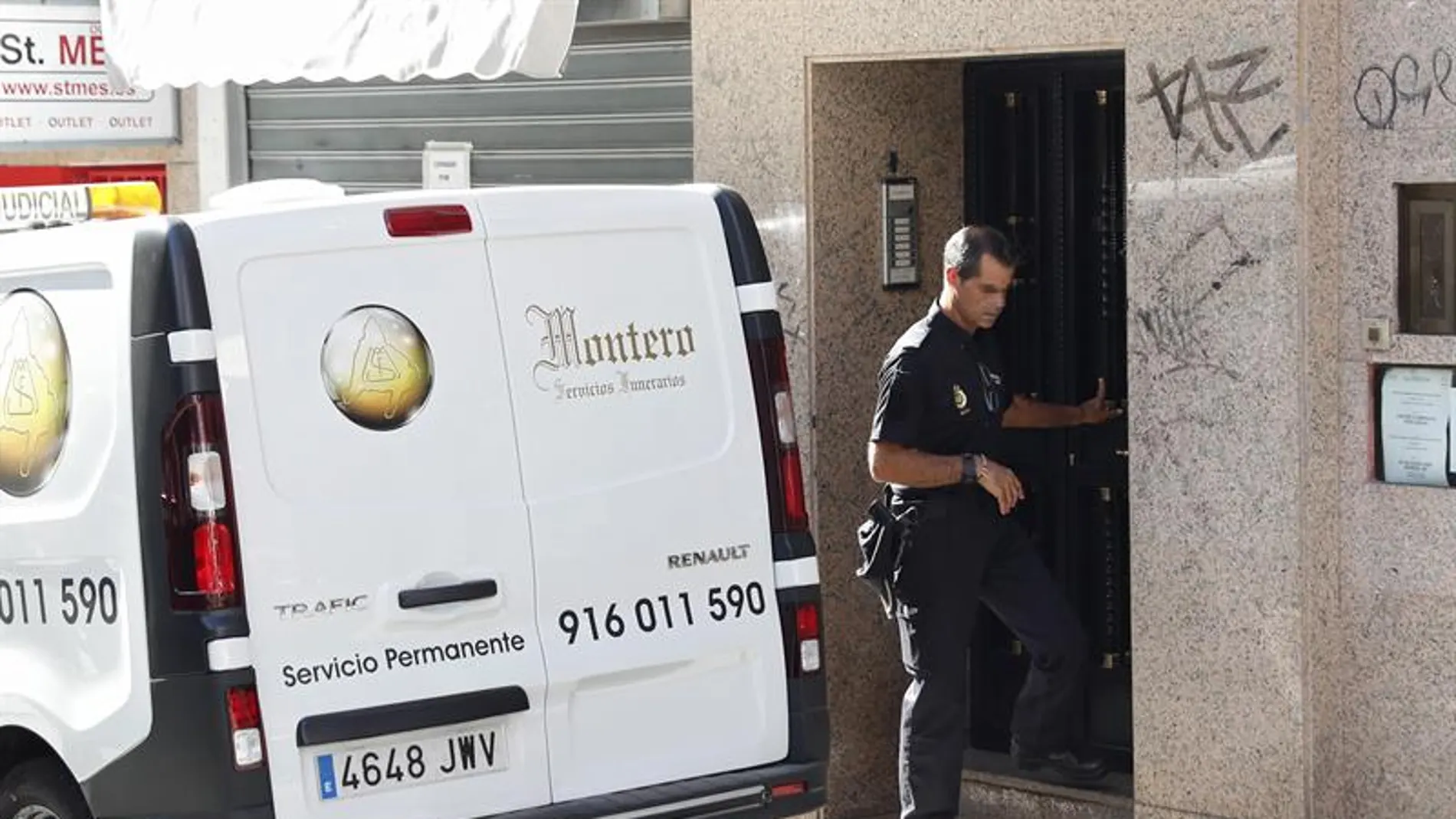 Un agente de la Policía Nacional junto a una furgoneta de los servicios funerarios en el domicilio de la mujer fallecida en Alcorcón Un agente de la Policía Nacional junto a una furgoneta de los servicios funerarios en el domicilio de la mujer fallecida en Alcorcón