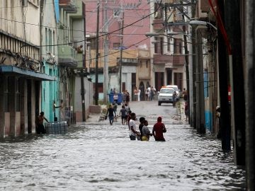  Varias personas caminan dentro del agua en una calle inundada de la capital cubana 