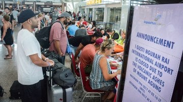 Turistas escuchan información sobre sus vuelos tras la erupción del volcán Agung en el aeropuerto Ngurah Rai en Denpasar en Bali (Indonesia)