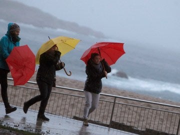 Tres mujeres se protegen de la lluvia en el paseo marítimo de A Coruña