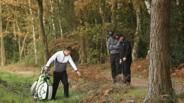 Un golfista consulta la posición de una bola a un árbitro durante un campeonato