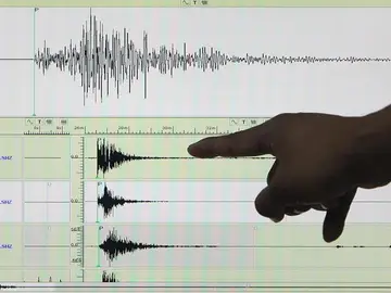 Un sismólogo señala un sismógrafo Un sismólogo señala un sismógrafo