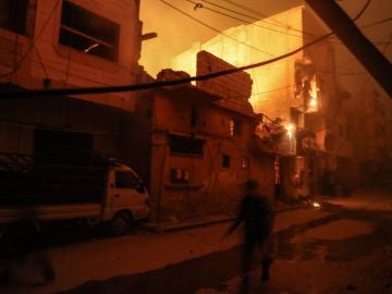 Personas caminan entre edificios en llamas después de presuntos ataques aéreos con fósforo blanco este viernes 