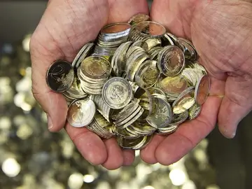 Un hombre sostiene varias monedas de euro Un hombre sostiene varias monedas de euro