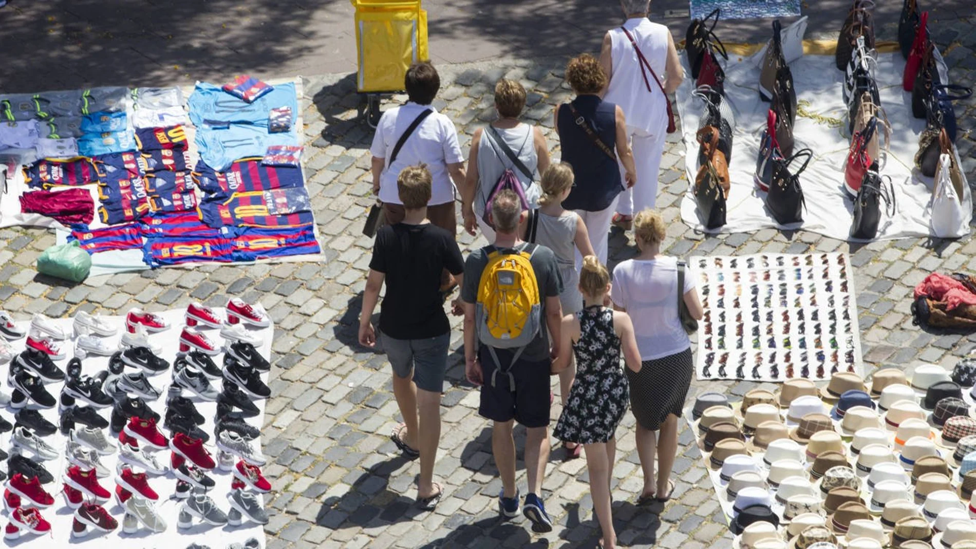 Unos turistas pasean por Las Ramblas de Barcelona entre varios manteros Unos turistas pasean por Las Ramblas de Barcelona entre varios manteros