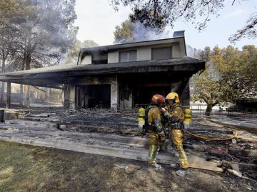 Dos bomberos ante una de las viviendas afectadas por el incendio forestal de Llutxent 