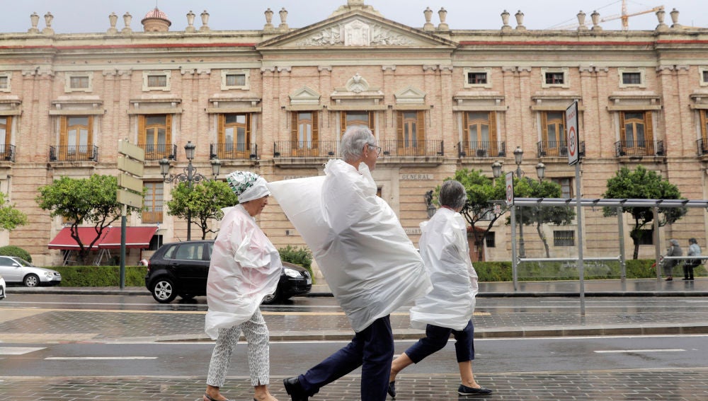 Tres personas se protegen con bolsas de plástico por las calles de Valencia