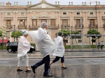 Tres personas se protegen con bolsas de plástico por las calles de Valencia