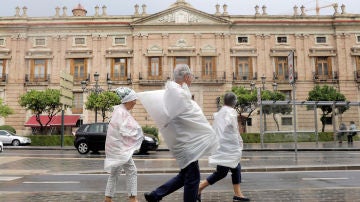 Tres personas se protegen con bolsas de plástico por las calles de Valencia