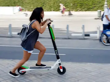 Una joven circulando en un patinete eléctrico Una joven circulando en un patinete eléctrico