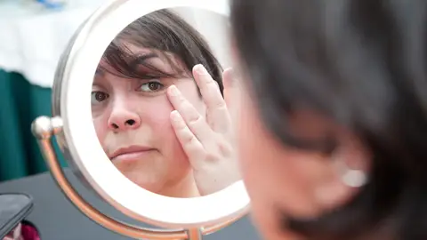 Mujer se mira la cara frente al espejo Mujer se mira la cara frente al espejo