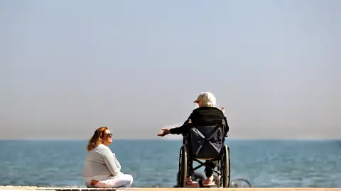 Dos mujeres conversan a orillas del mar mientras disfrutan del sol Dos mujeres conversan a orillas del mar mientras disfrutan del sol