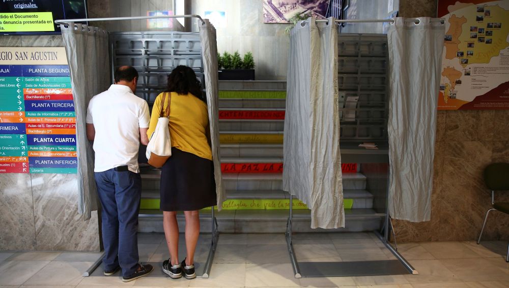 Dos personas eligen sus papeletas para votar en un colegio electoral