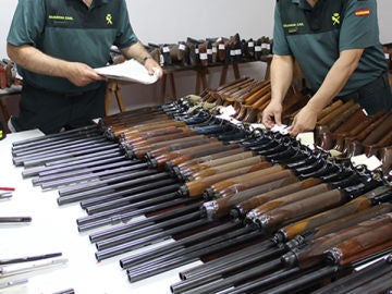 Dos agentes de la Guardia Civil revisan numerosas escopetas y armas