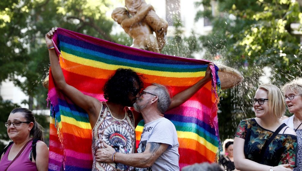 Dos hombres besándose ante la bandera del orgullo gay