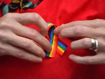Una persona poniéndose un lazo LGTBI Una persona poniéndose un lazo LGTBI