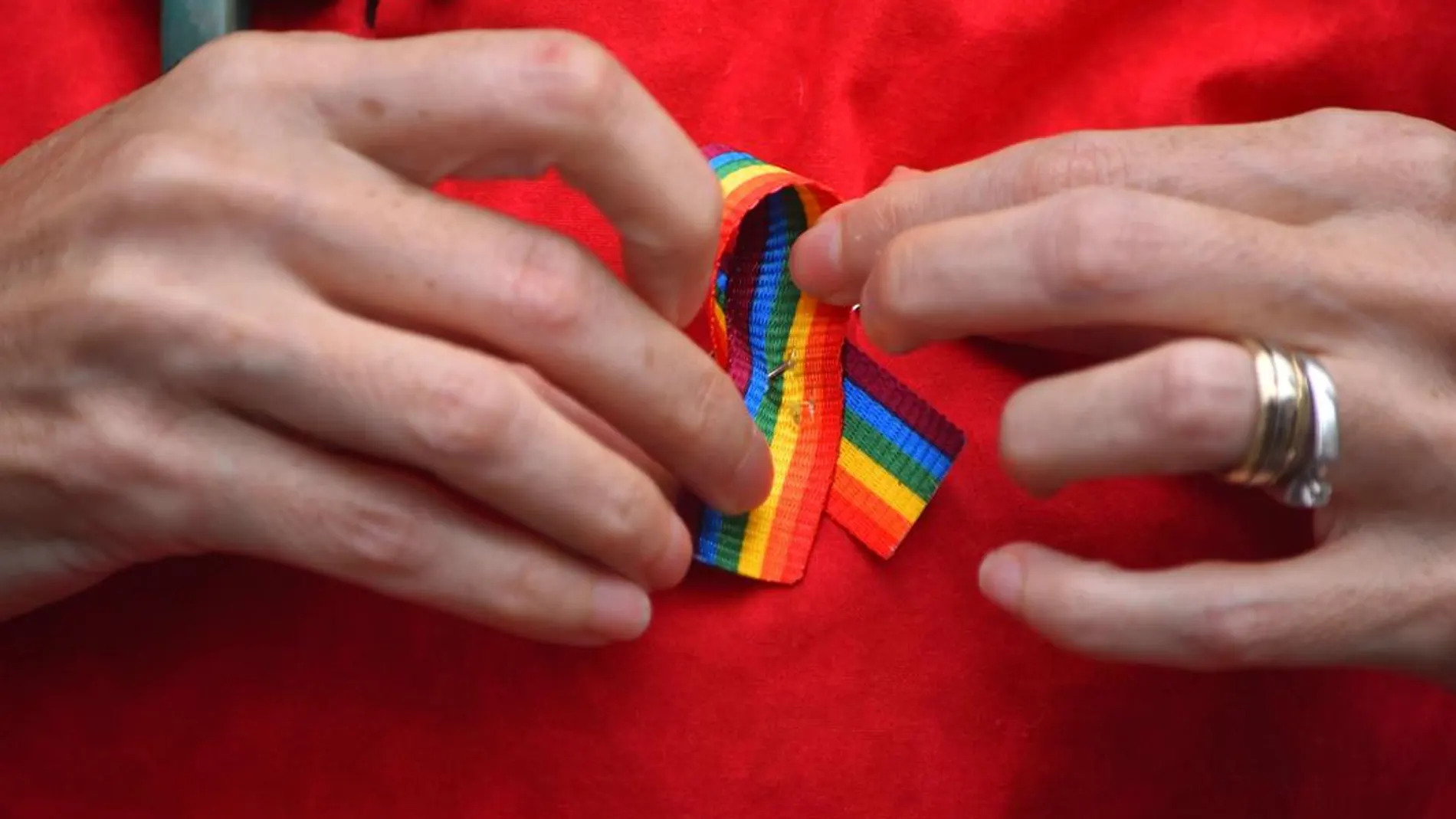 Una persona poniéndose un lazo LGTBI Una persona poniéndose un lazo LGTBI