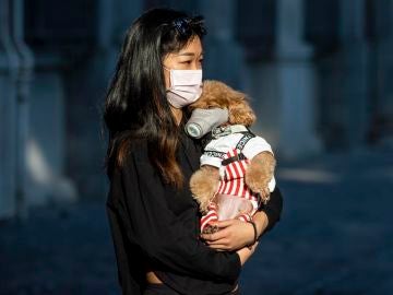 Mujer llevando a su perro con mascarilla