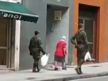 Dos militares ayudan a una anciana a llevar la compra a casa en Gijón durante la cuarentena por coronavirus