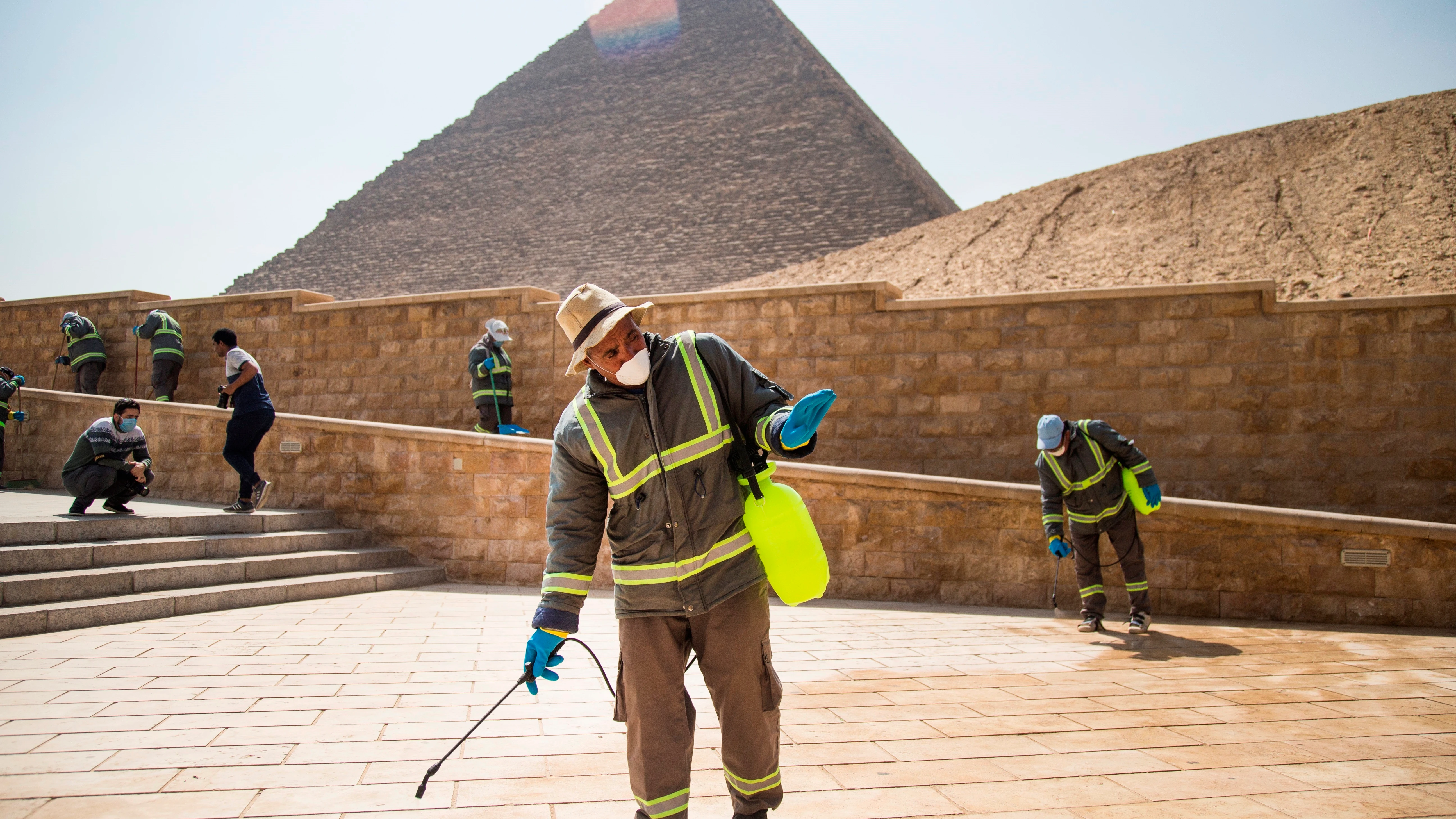 Varias personas desinfectan las inmediaciones de las pir&aacute;mides de Giza en El Cairo
