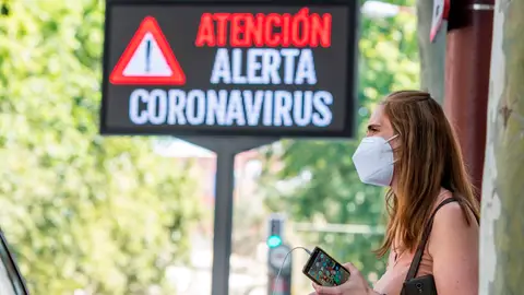 Una mujer espera el autobús junto a un panel informativo en Sevilla Una mujer espera el autobús junto a un panel informativo en Sevilla