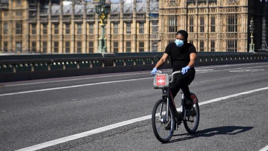 Un hombre con mascarilla circula en bicicleta frente al Parlamento brit&aacute;nico en Londres