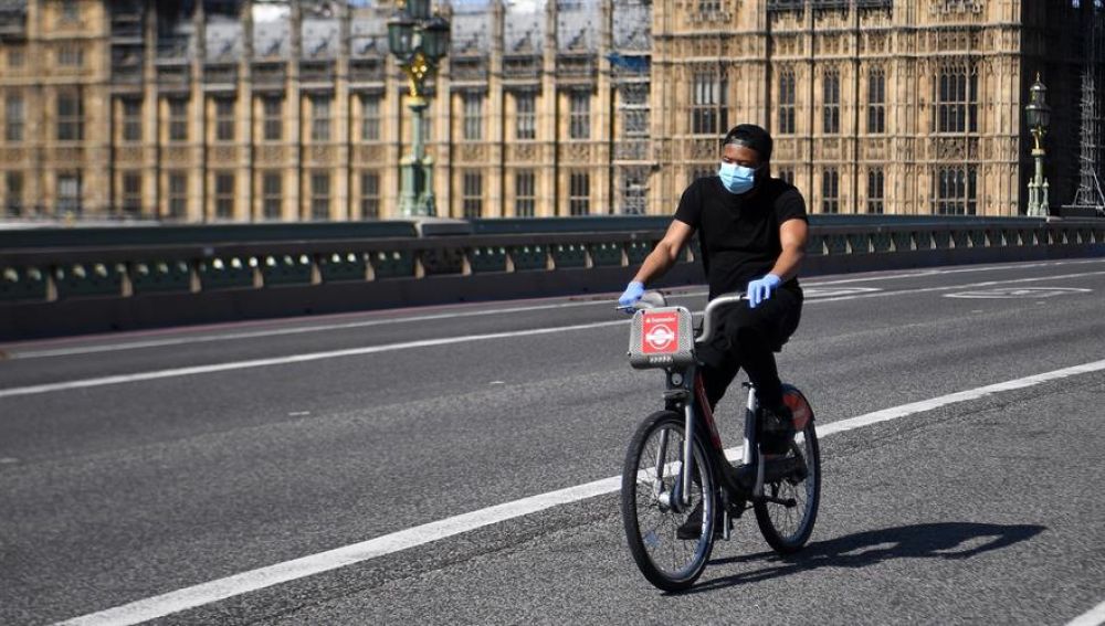 Un hombre con mascarilla circula en bicicleta frente al Parlamento británico en Londres