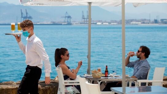Un camarero con mascarilla pasa ante una pareja que almuerza en un restaurante de M&aacute;laga