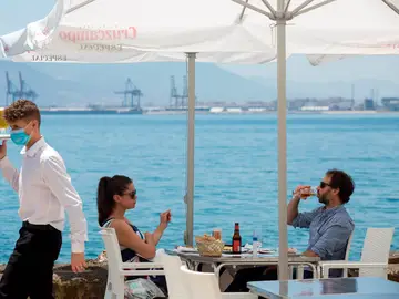 Un camarero con mascarilla pasa ante una pareja que almuerza en un restaurante de Málaga
