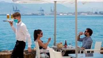 Un camarero con mascarilla pasa ante una pareja que almuerza en un restaurante de Málaga