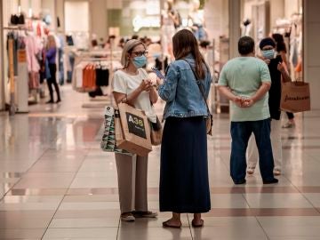 Varias personas realizan compras en un centro comercial con mascarillas.