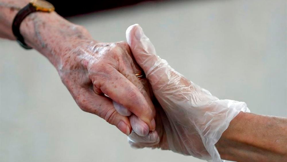 Una sanitaria da la mano a una anciana en una residencia