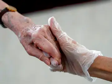 Una sanitaria da la mano a una anciana Una sanitaria da la mano a una anciana