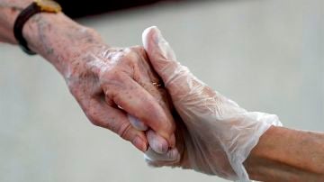 Una sanitaria da la mano a una anciana en una residencia