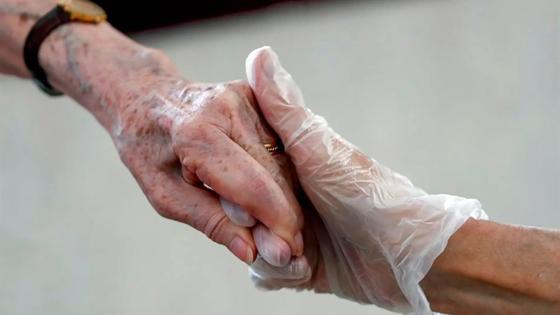 Una sanitaria da la mano a una anciana