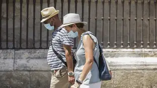 Dos personas caminan con mascarilla y sombrero Dos personas caminan con mascarilla y sombrero