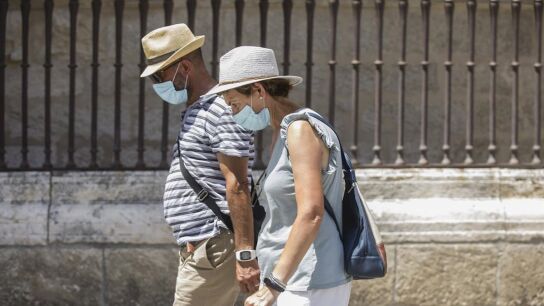 Dos personas caminan con mascarilla y sombrero