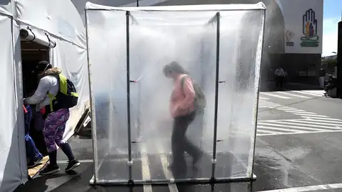 Personas pasan por una cabina de desinfección de coronavirus coronavirus