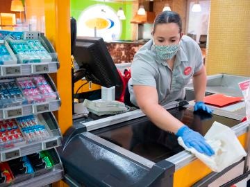 Una empleada de un supermercado desinfecta la caja