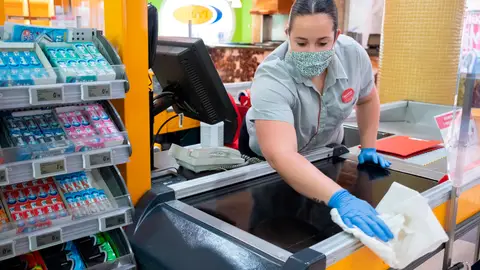 Una empleada de un supermercado desinfecta la caja Una empleada de un supermercado desinfecta la caja