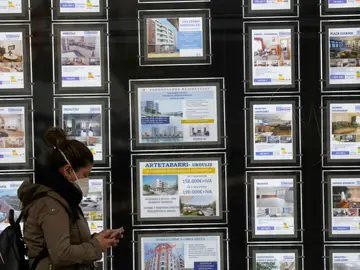 Una mujer pasa por delante de un portal inmobiliario de venta y alquiler Una mujer pasa por delante de un portal inmobiliario de venta y alquiler