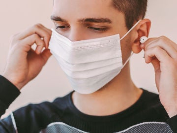 Un joven con mascarilla usa auriculares