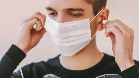 Un joven con mascarilla usa auriculares Un joven con mascarilla usa auriculares