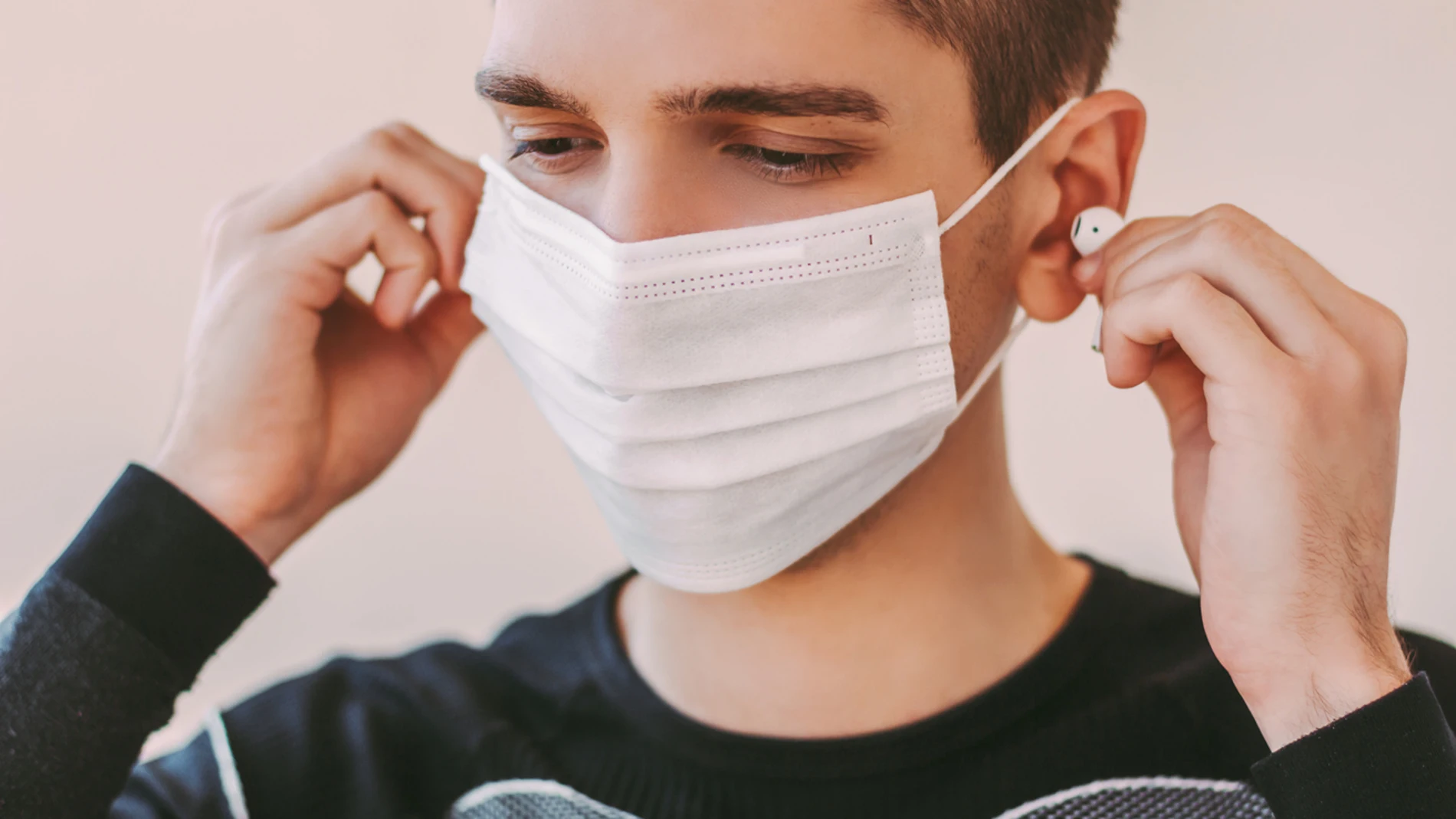 Un joven con mascarilla usa auriculares Un joven con mascarilla usa auriculares