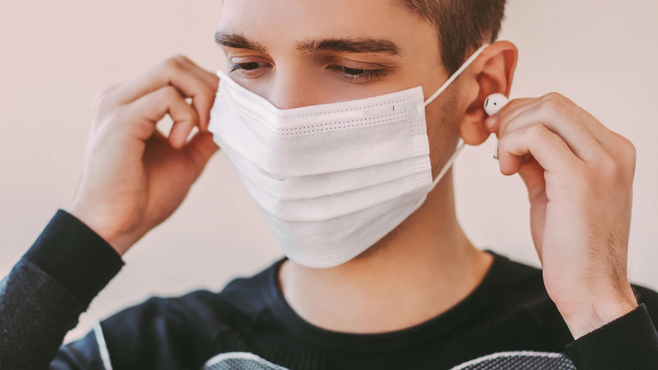 Un joven con mascarilla usa auriculares Un joven con mascarilla usa auriculares