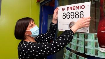 La propietaria de la administración de lotería 81 de Zaragoza coloca el cartel tras haber vendido décimos del número 86986 uno de los quintos premios