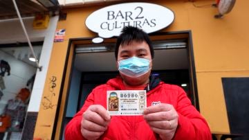 Juan, propietario del bar Dos Culturas de Zaragoza, muestra uno de los décimos agraciados con el quinto premio 86986 del Sorteo Extraordinario de Navidad