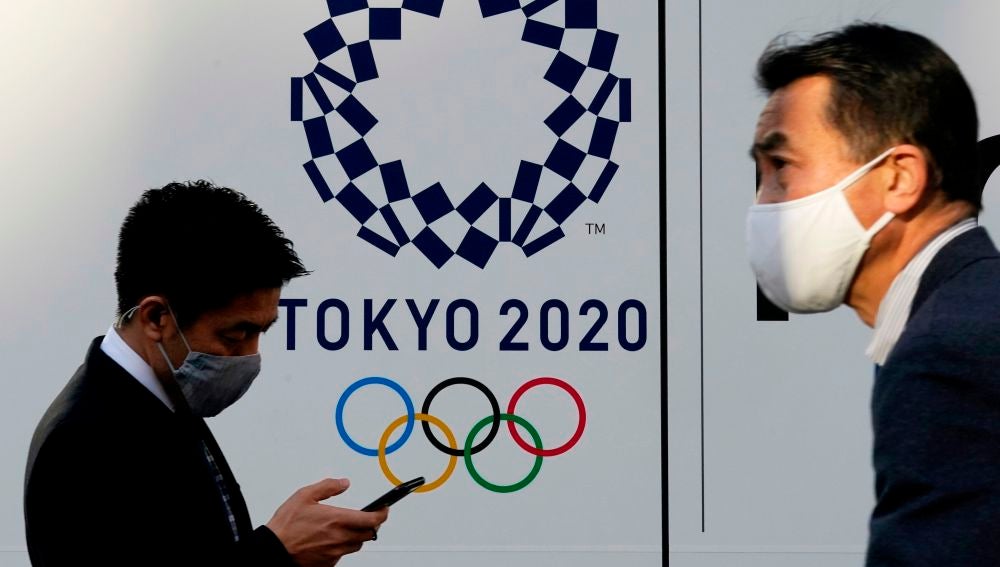 Dos personas pasean con el logo de los Juegos Olímpicos de Tokio 2020 de fondo.
