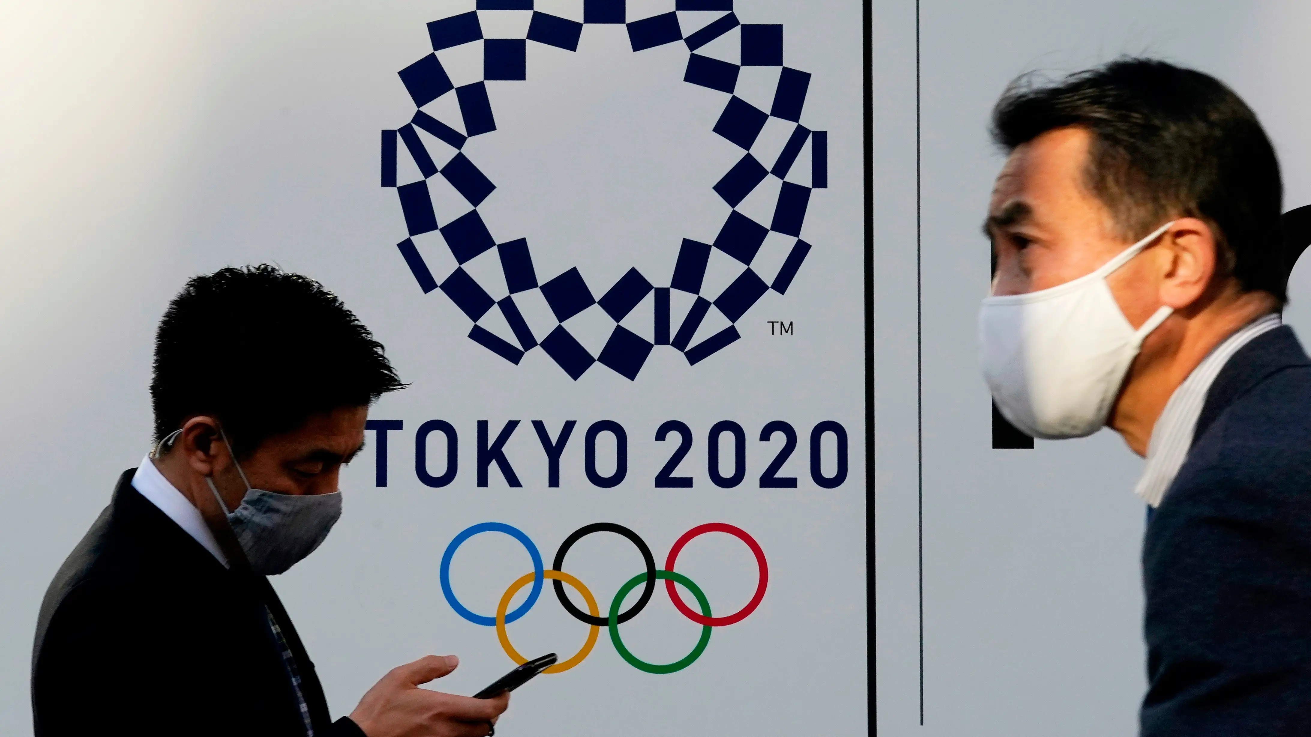 Dos personas pasean con el logo de los Juegos Olímpicos de Tokio 2020 de fondo. Dos personas pasean con el logo de los Juegos Olímpicos de Tokio 2020 de fondo.